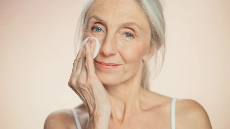 medium potrait  beautiful senior woman uses cotton wool pad to clean her perfect face of cosmetics smiling elderly lady with soft skin graceful old age and natural skincare cleansing product