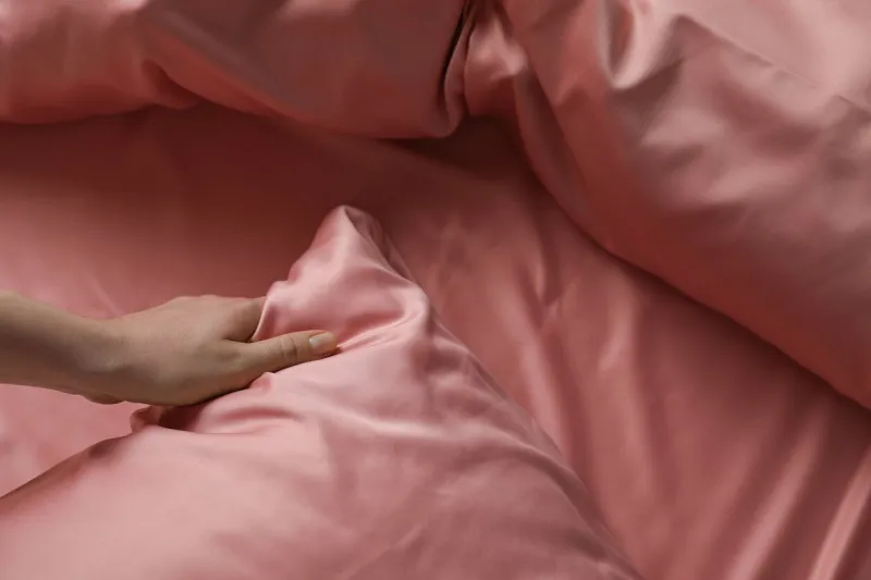 woman making bed with beautiful pink silk linens, closeup view