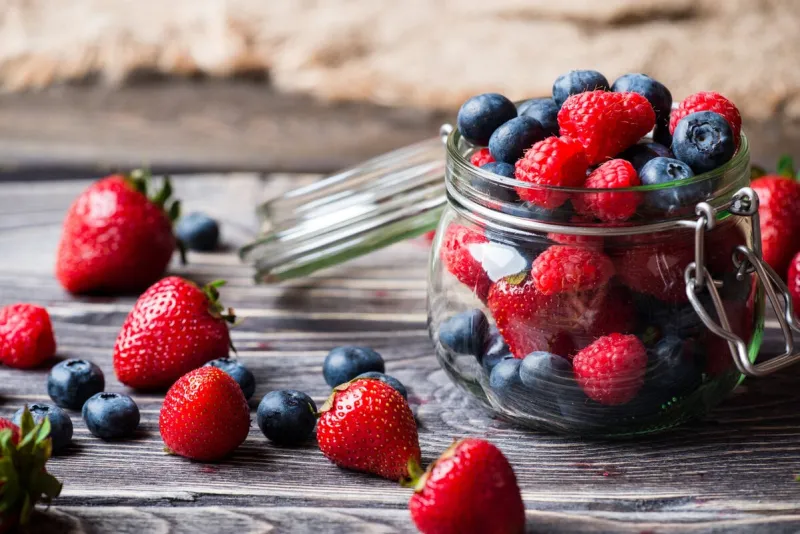 berries in glass jar, over wooden background strawberries, raspberries, blueberry
