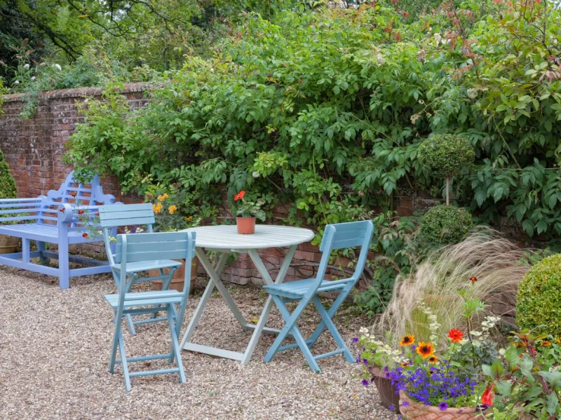 blue bench, patio table and chairs by a wall in an english cottage garden, summertime