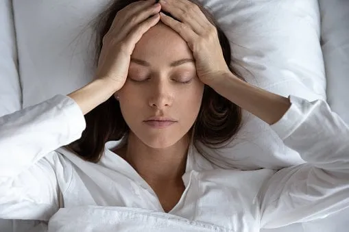 top view close up depressed woman suffering from headache or migraine, touching forehead with hands, lying in bed with closed eyes, unhappy young female feeling bad, pain in head, hangover