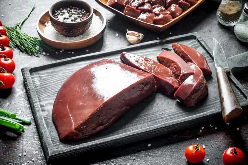 sliced raw liver with tomatoes, herbs and spices on dark rustic background