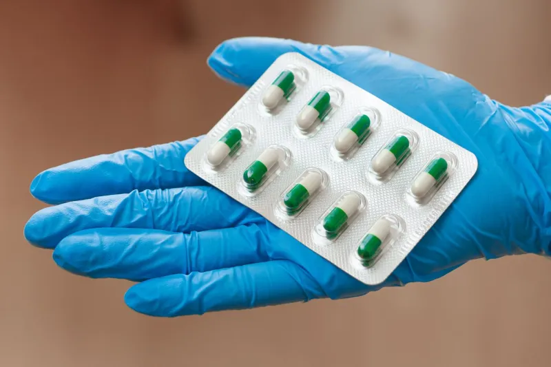 pills in woman hand in blue gloves vitamins or medicine for coronavirus treatment