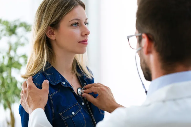 shot of handsome young male doctor checking beautiful young woman patient heartbeat using stethoscope in medical office