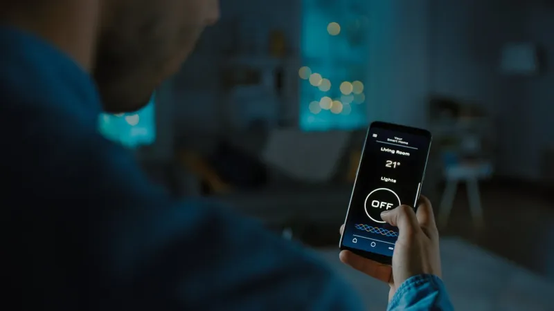 close up shot of a smartphone with active smart home application person is tapping the screen and light is being turned on in the room it's cozy evening in the apartment