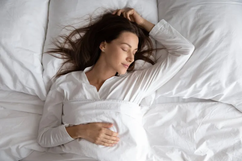 peaceful serene beautiful young lady wear pajamas lying asleep relaxing sleeping in cozy white bed on soft pillow resting covered with blanket enjoying good healthy sleep concept, above top view