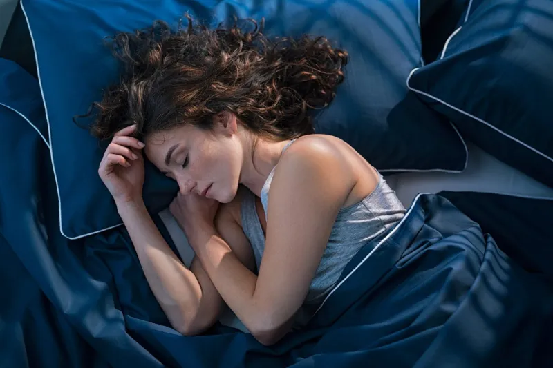 top view of young woman sleeping on side in her bed at night beautiful girl sleeping profoundly and dreaming at home with blue blanket high angle view of woman asleep with closed eyes