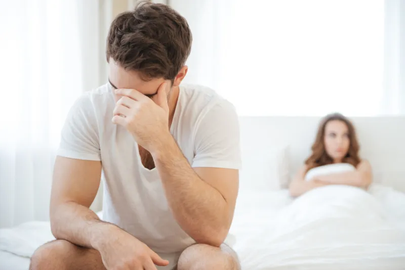 depressed young man sitting on bed and having problems with his girlfriend