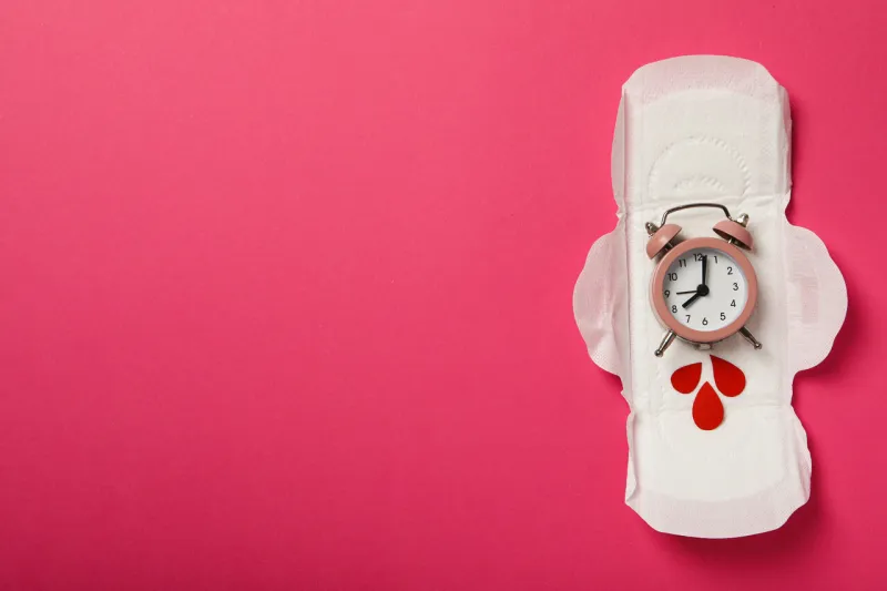 menstrual pad with clock and red drops on pink background