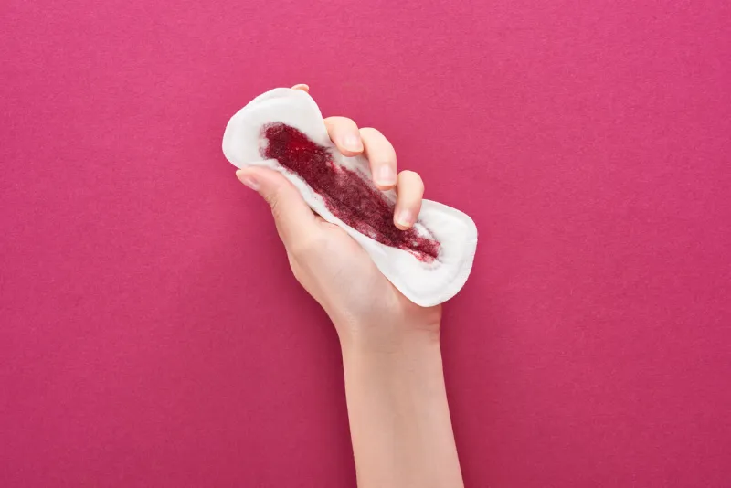 partial view of woman holding sanitary towel with blood on purple background