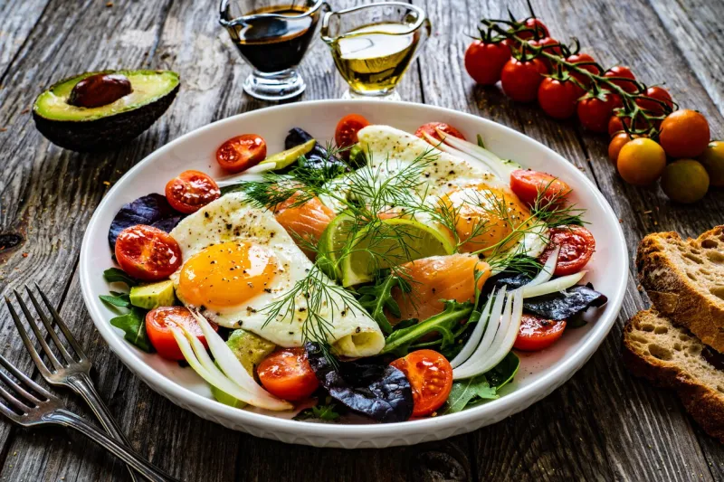 smoked salmon with sunny side up eggs, avocado and leafy vegetables on wooden table