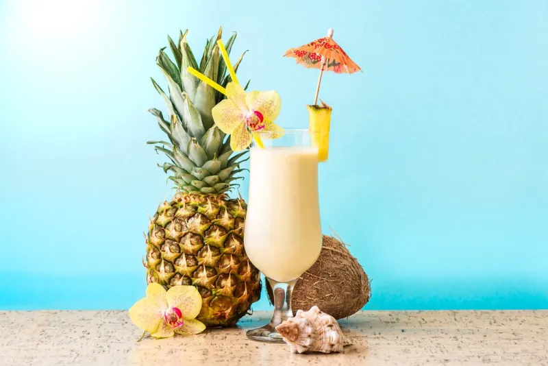 pina colada cocktail drink with pineapple and coconut, blue background, copy space summer tropical delicious cocktail with fruits and flowers, vacation concept
