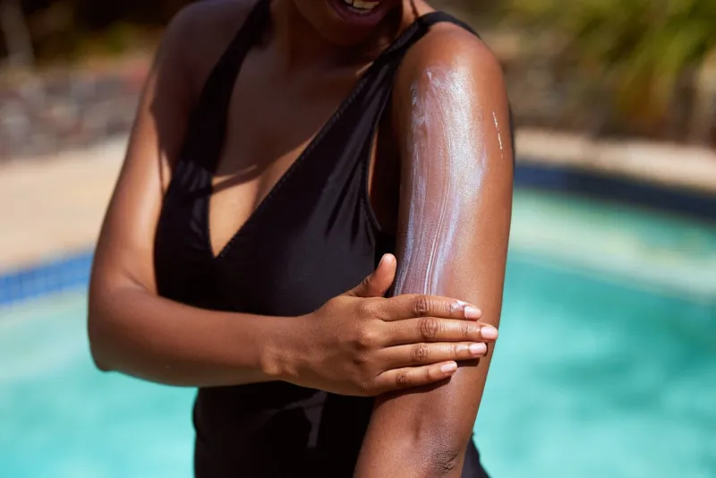 close up of black woman spreading sunscreen onto arm with pool background high quality photo