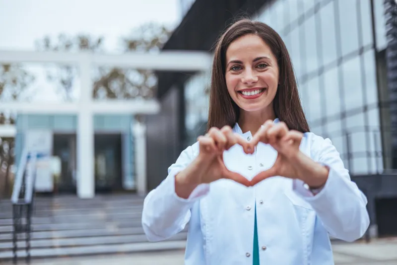 closeup woman nurse making a heart shape with her hands while smiling and standing in hospital take care of your heart and love your body health and safety in the field of medicine