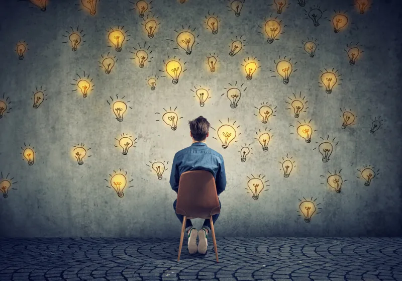 man sitting on a chair has many bright ideas looking at wall making decisions