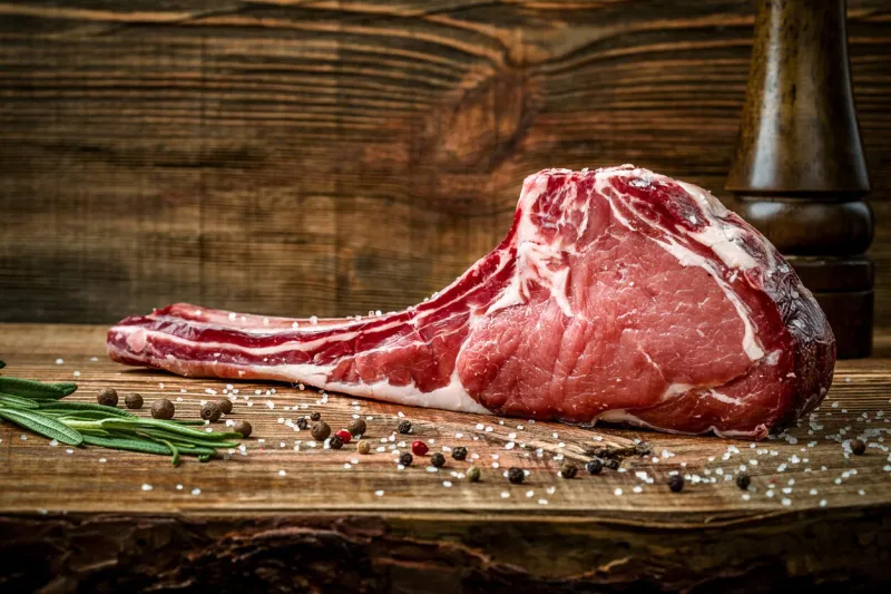 dry aged raw tomahawk beef steak with spices on a wooden background ingredients for grilling