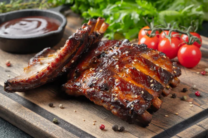 closeup of pork ribs grilled with bbq sauce and caramelized in honey tasty snack to beer on a wooden board for filing on dark concrete background