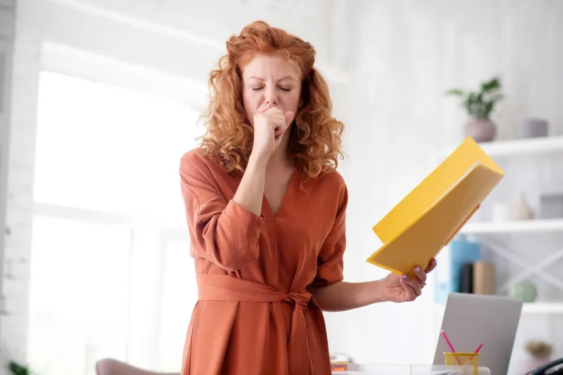 woman coughing curly red-haired woman coughing because of flu while working