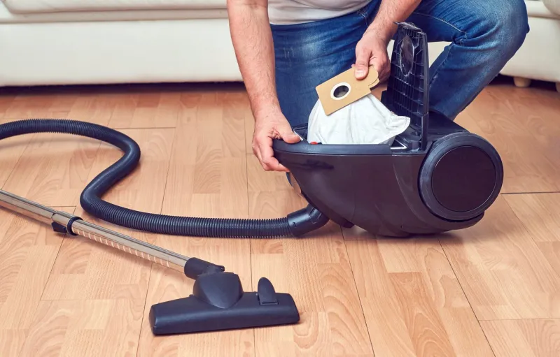 man taking out a full dust bag from a vacuum cleaner