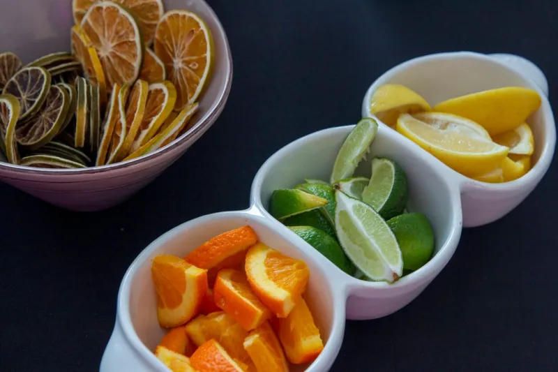 a vibrant arrangement of freshly sliced oranges, lemons, and limes is displayed in white bowls, alongside a bowl of dried lemon slices, perfect for garnishing or snacking