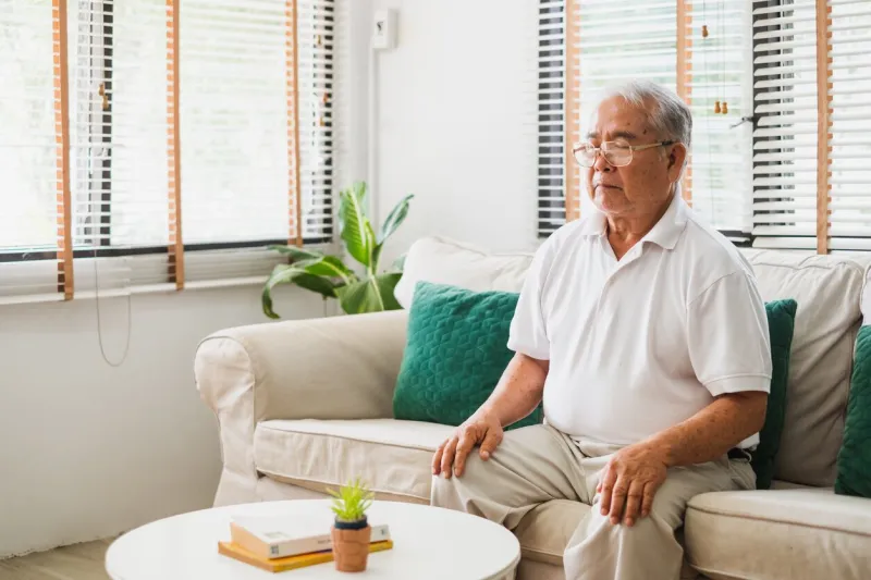 senior old asian man sitting on sofa praticing yoga and meditation at home, retirement and wellbeing concept