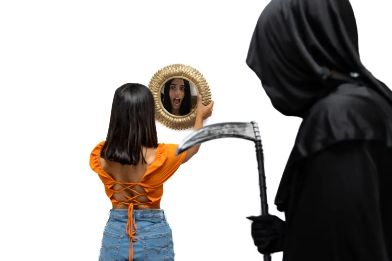 terrified young woman, viewed from behind and reflected in a mirror, is confronted by the grim reaper, dressed in a halloween costume with dark cloak, as he menacingly holds a scythe white background