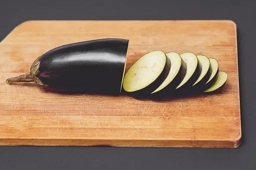 sliced eggplants fresh and raw on a wooden cutting board on the black background close up