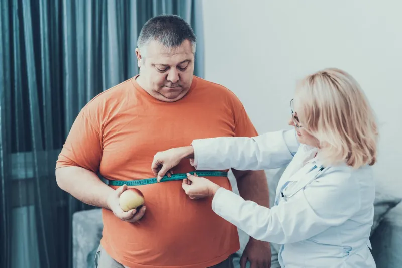 fat man with doctor in white coat in gray room woman with tailors centimeter diet and healthcare concept man with bulimia unhealthy lifestyle concept man with overweight patient with stomach