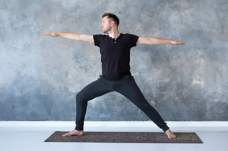 young man practicing yoga in studio doing warrior 2 pose, viradhadrasana