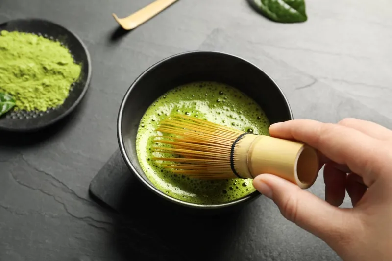 woman preparing matcha tea at black table, above view