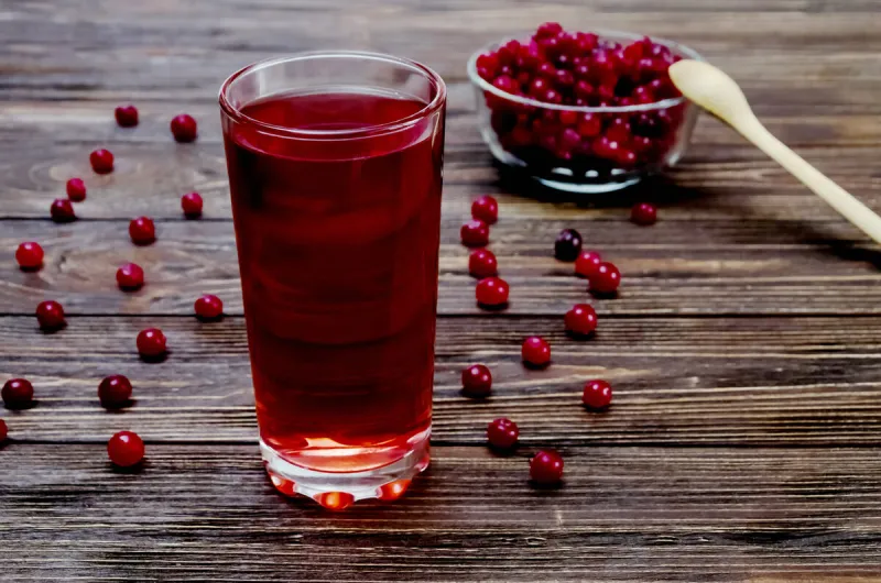 cranberry and drink in glass glass on brown wooden background
