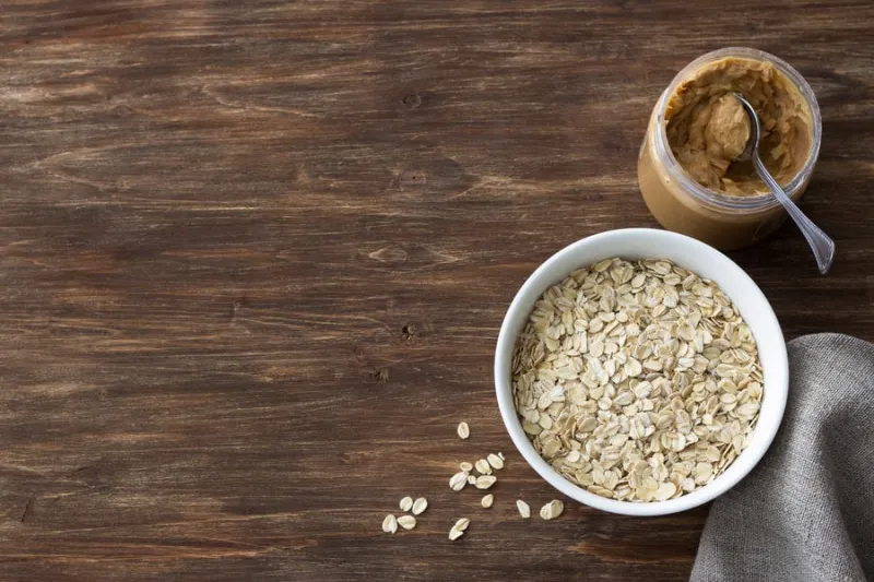 raw oatmeal in a white bowl with peanut butter, ingredients for a delicious healthy breakfast on a wooden background, top view, free space, horizontal