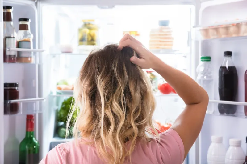 rear view of a confused woman looking in open refrigerator at home