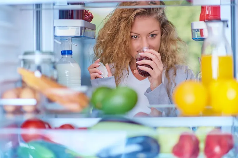 woman smelling jam in front of fridge full of groceries picture taken from the inside of fridge
