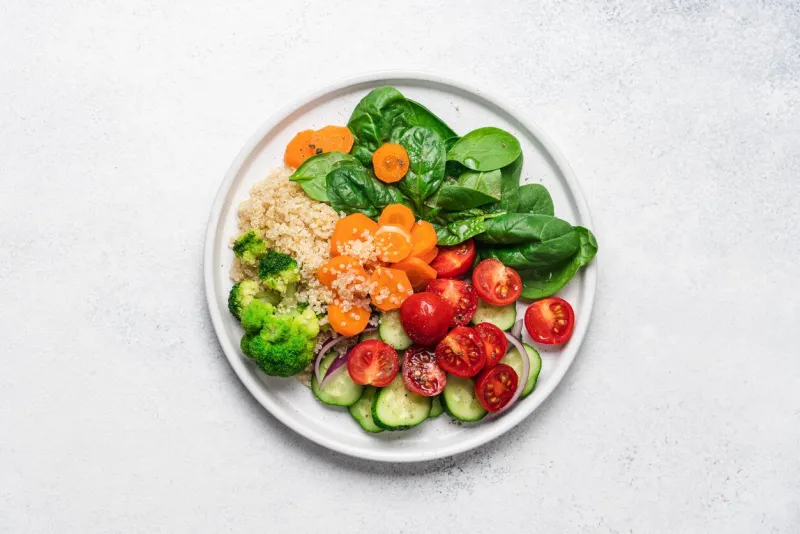 salad with quinoa, spinach, broccoli, tomatoes, cucumbers and carrots, served on plate with white background and copy space clean healthy food concept