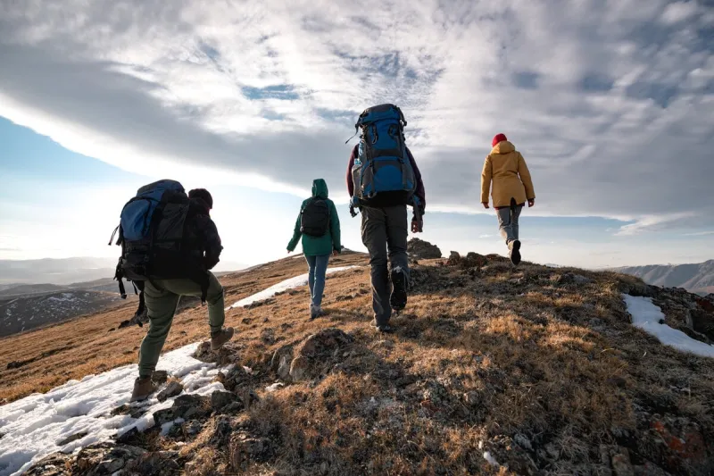 group of four diverse tourists or hikers are walking on mountain top at sunset time