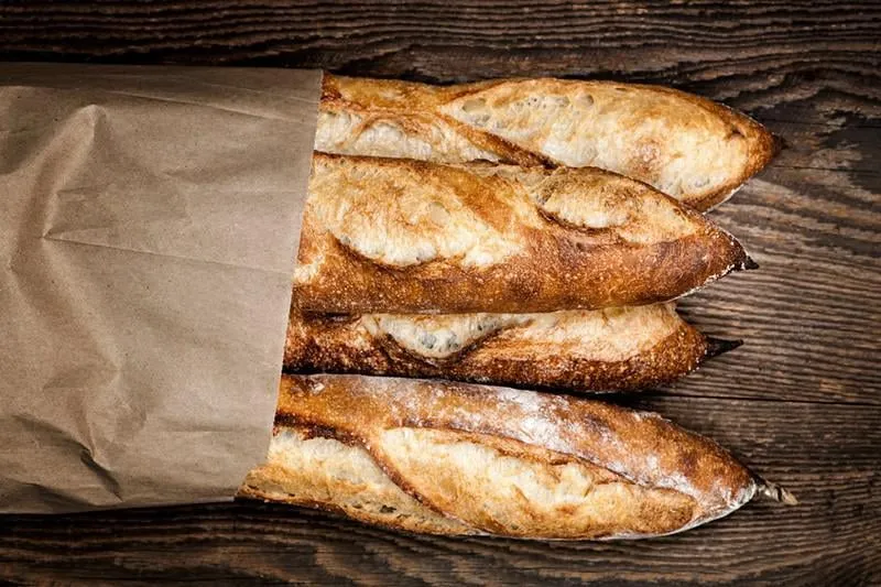 quatre pains baguette baguette dans un sac en papier sur fond en bois