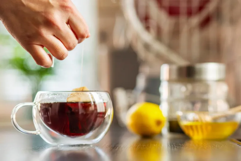 woman puts the tea bag in the glass cup with hot water woman brews tea using a tea bag