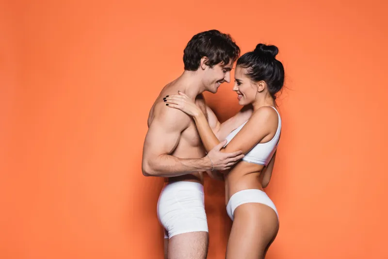 side view of happy and sexy couple in white underwear standing on orange,stock image