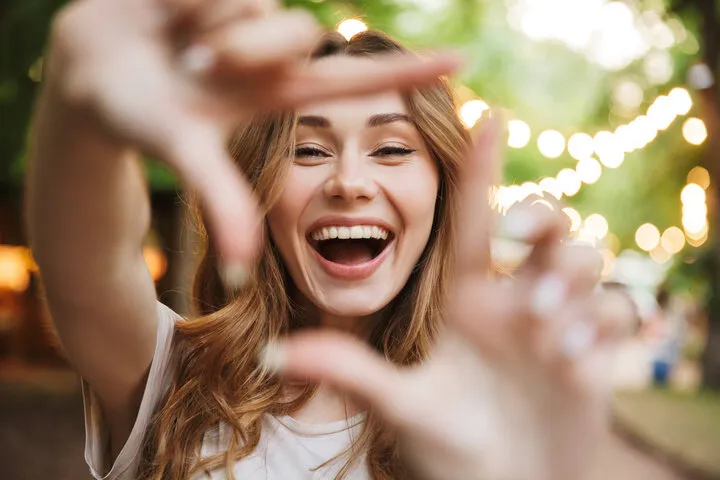 close up of happy young girl showing frame with fingers while standing at the park