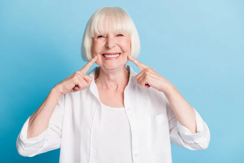 photo portrait of granny blonde hair pointing at white teeth healthy smile dental whitening veneers isolated on bright blue color background