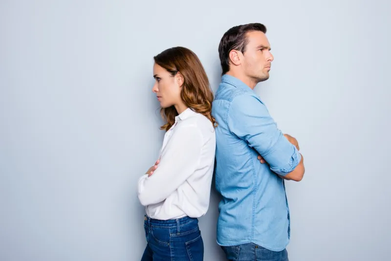 portrait of unhappy frustrated couple standing back to back not speaking to each other after an argument while standing on grey background negative emotion face expression reaction