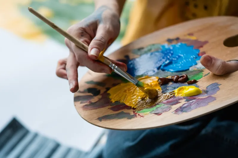 fine art school closeup of artist hands holding wooden palette, mixing acrylic paint with brush