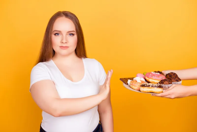 i'm against eating products containing fat will-powered woman wearing white tshirt is refusing to consume tasty delicious sweets on a plate, isolated on bright yellow background