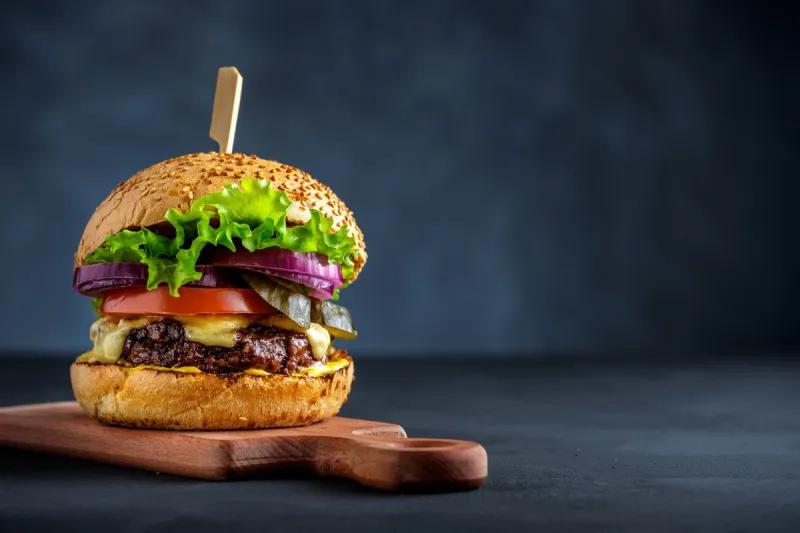 tasty grilled beef burger with lettuce, cheese and onion served on cutting board on a black wooden table, with copyspace
