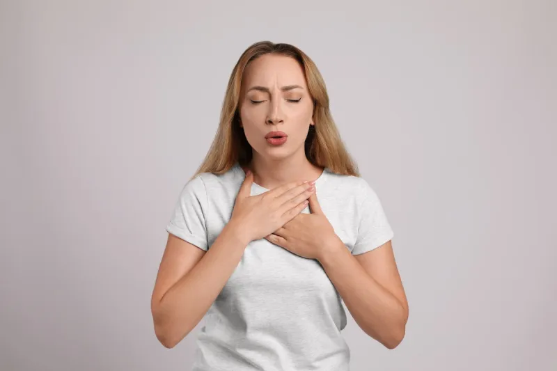 young woman suffering from pain during breathing on light grey background