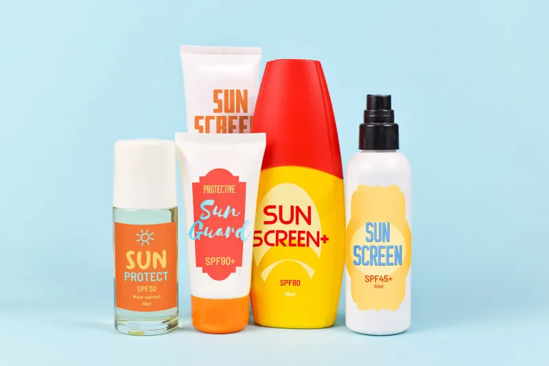 different protective sun screen cream bottles and spray tubes with made up labels on light blue background