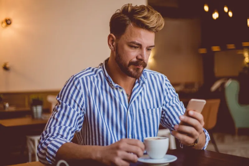 bearded millennial guy using phone at coffee shop
