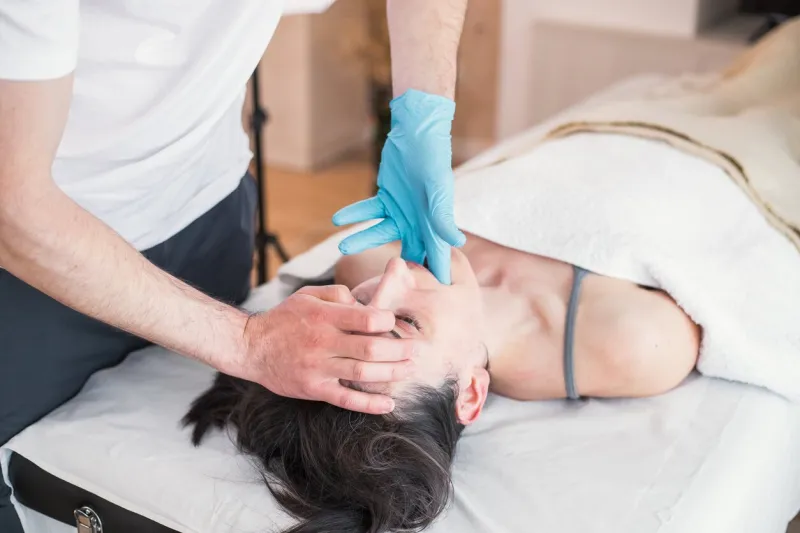 osteopathic therapist doing treatment to caucasian woman with jaw problem, mandibular alignment treatment to relieve pain and improve the patient's health conditions