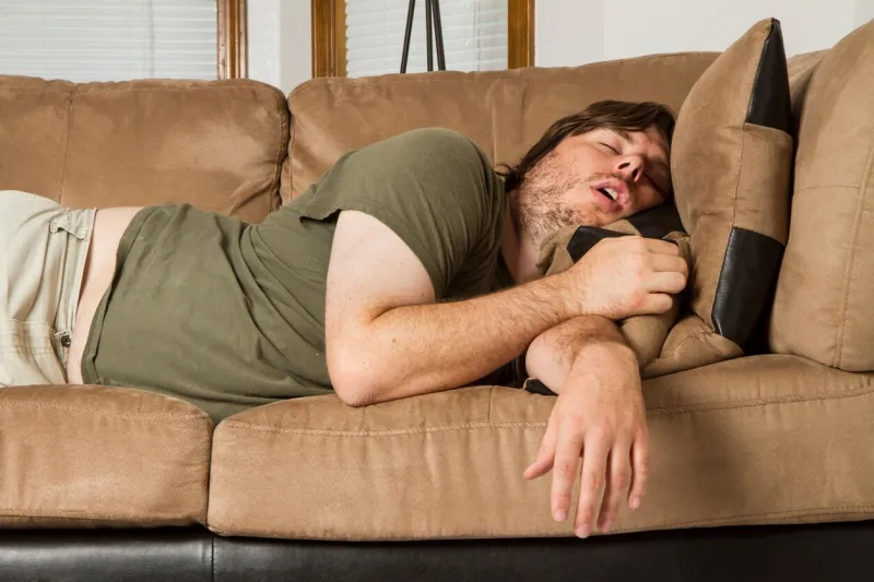 fat guy sleeping on the couch in what looks like an uncomfortable position